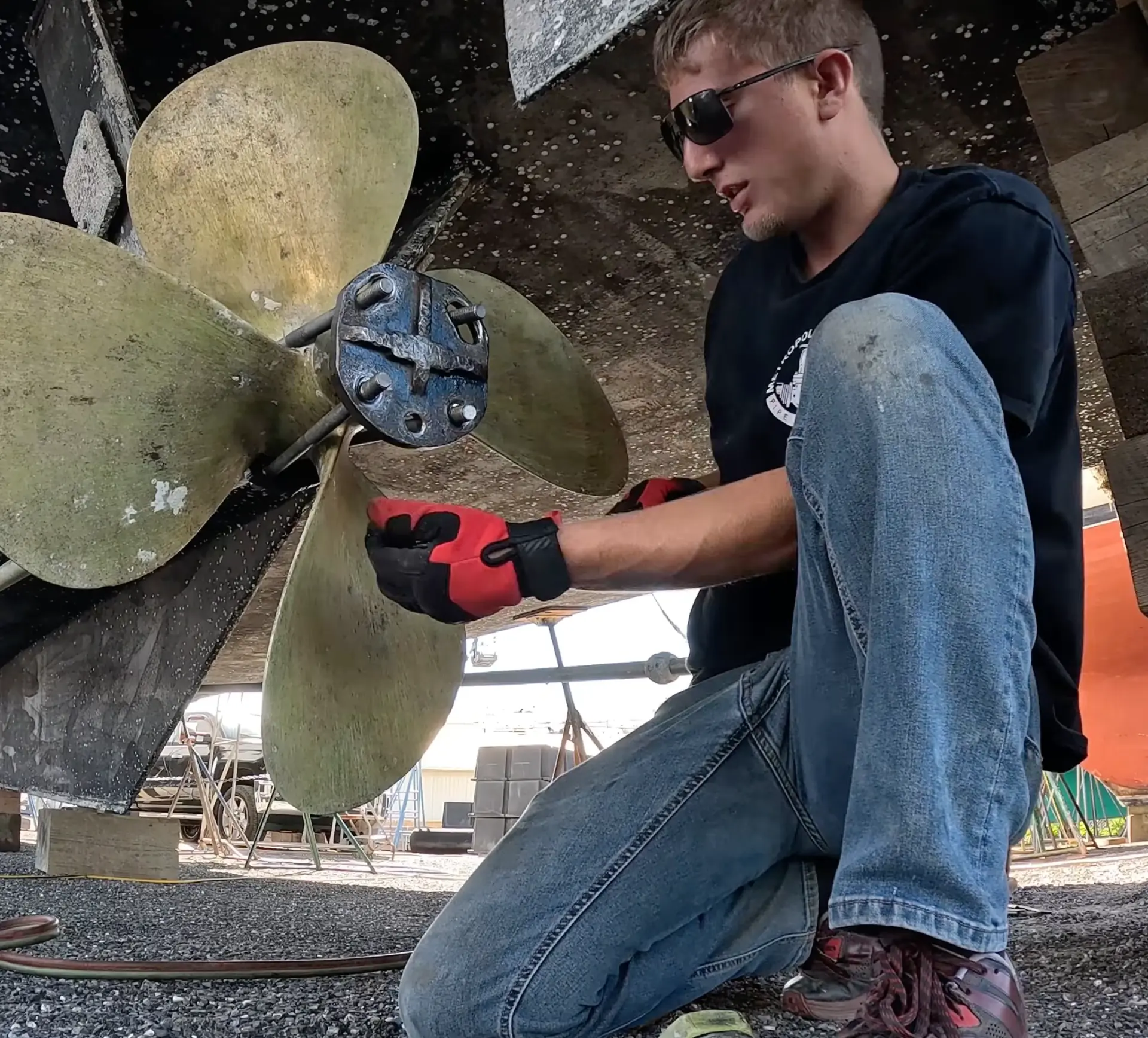 Gus kneeling beside a boat propeller under the hull in dry dock